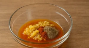Transparent bowl showing spices, saffron water, garlic, and preserved lemon pulp prepared for Moroccan beef tagine marinade.