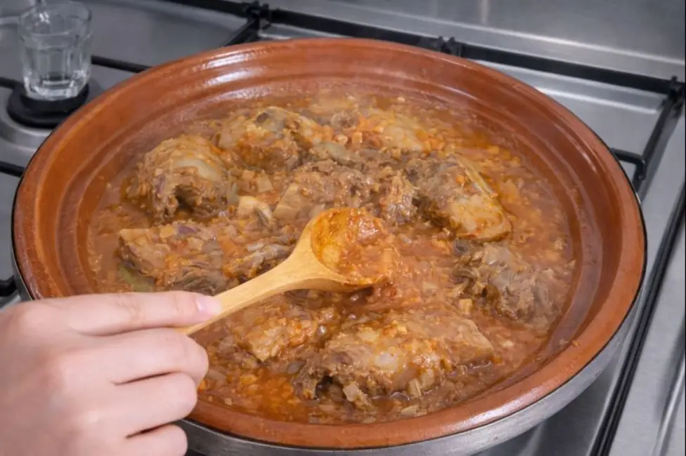 A traditional Moroccan tagine with beef and green beans simmering slowly after water is added, stirred gently by hand.