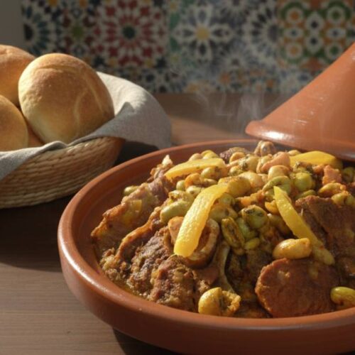 Steaming Moroccan beef tagine with preserved lemons and olives in a clay pot next to bread.