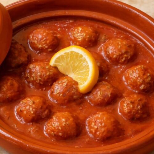 Moroccan meatballs simmering in a rich tomato sauce within a traditional tagine.