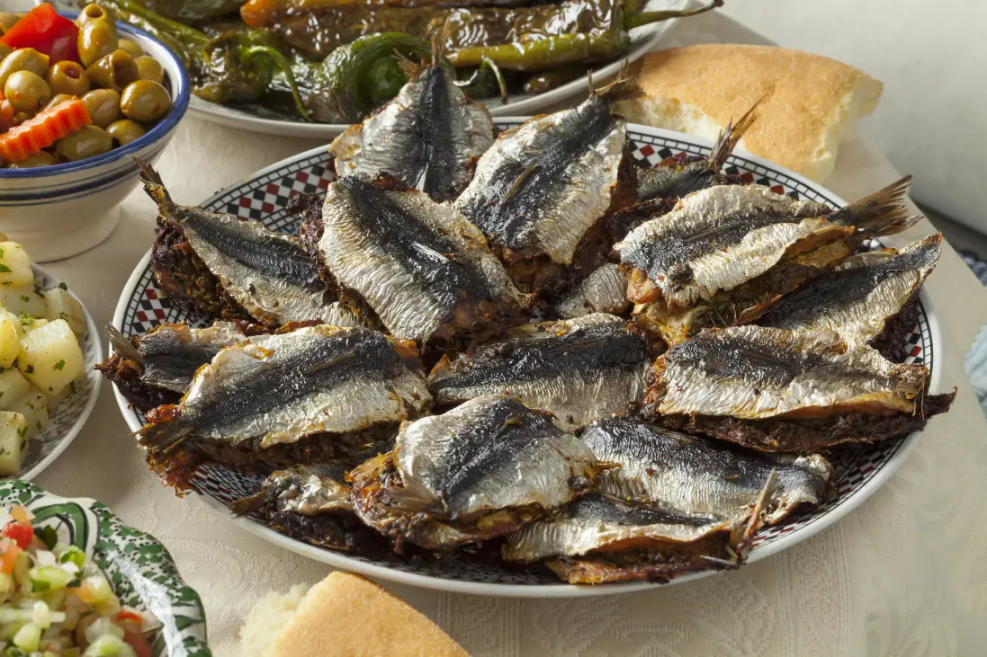 Moroccan fish dishes.A platter of traditional Moroccan stuffed sardines, served alongside bowls of olives, roasted peppers, potato salad, and Moroccan bread on a white tablecloth.