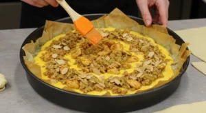 Hands layering Moroccan Bastilla with phyllo, chicken, eggs, and almonds in a round dish.