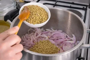 Pouring lentils into a pot for rfissa recipe with onions on a stove