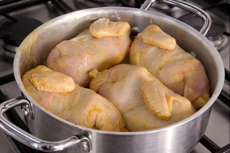 Close-up of four Cornish hens cooking in a large silver pot on a stovetop, part of the preparation of Rfissa, a typical Moroccan meal.