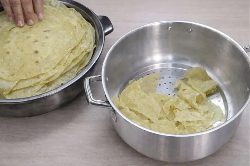 two stainless steel dishes on a light wooden surface; one contains stacked trid flatbreads, while the other contains pieces of torn trid ready for Rfissa.