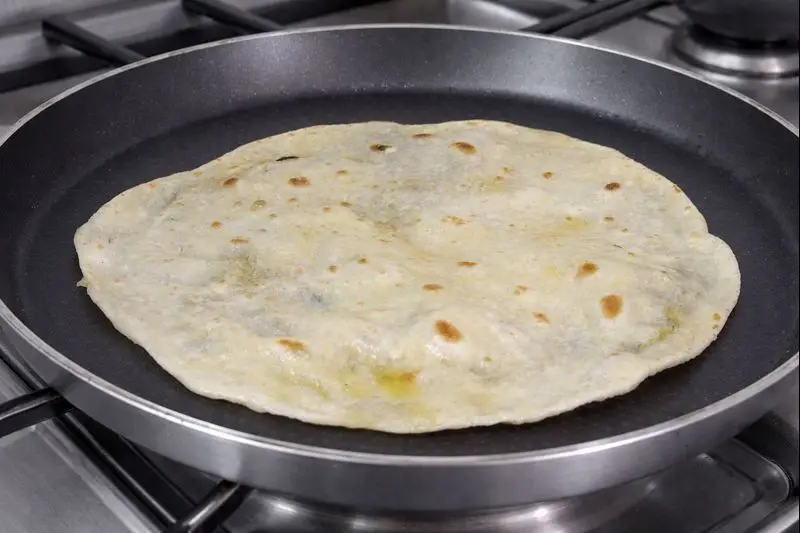 Close-up of a Moroccan Trid sheet with golden brown spots cooking in a silver pan on a stovetop.