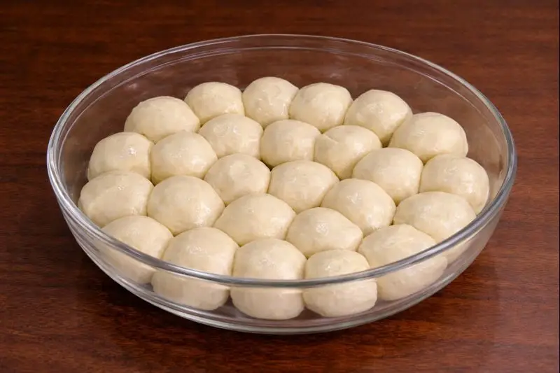 A clear round glass bowl filled with small, smooth, oiled dough balls arranged neatly — a preparation step for trid in the Moroccan dish Rfissa.