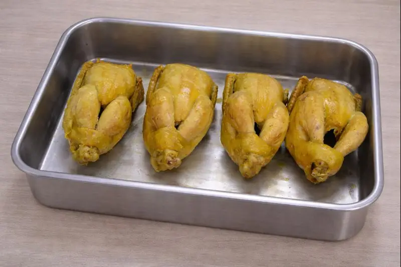 Four golden Cornish hens roasting in a stainless steel pan, part of the Rfissa preparation for a typical Moroccan meal.