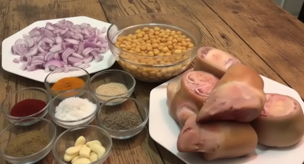 Fresh ingredients for Hargma tagine food arranged on a wooden table: clean calf trotters, soaked chickpeas, chopped red onions, garlic cloves, and bowls of Moroccan spices.