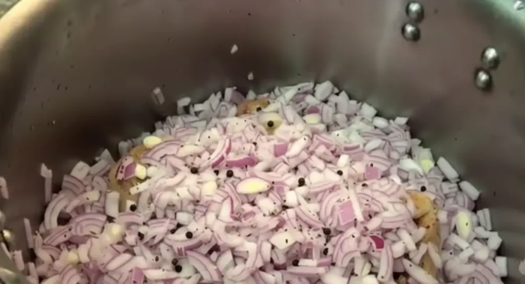Chopped red onions, garlic cloves, and Moroccan spices layered generously over raw calf trotters inside a pressure cooker, illustrating the dry "Cold Assembly" of tagine food.