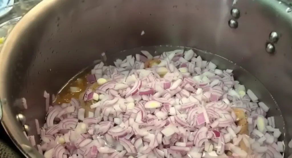 Pressure cooker filled with calf trotters, covered with chopped red onions, garlic, spices, and submerged in boiling water, ready for the first stage of tagine food cooking.