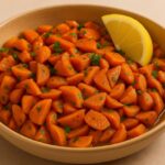 Moroccan carrot salad served in a beige bowl with a lemon wedge, featuring cooked carrots, parsley, and Moroccan spices