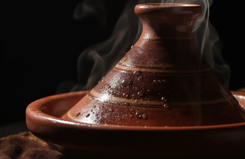 Close-up of a traditional clay tagine pot used for a Moroccan tagine recipe, with condensation and steam showing the slow-cooking process.