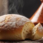 A perfectly golden-brown, freshly baked loaf of Moroccan bread, with a piece torn off to show the soft crumb.